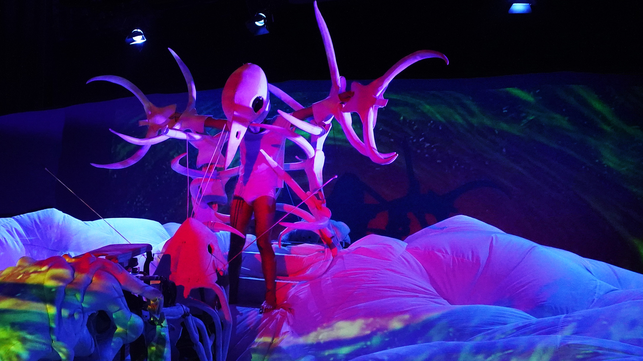 Snuff Puppets Swamp, a perosn covered in large white bones stands on top of a large inflatable mound covered in colourful projections