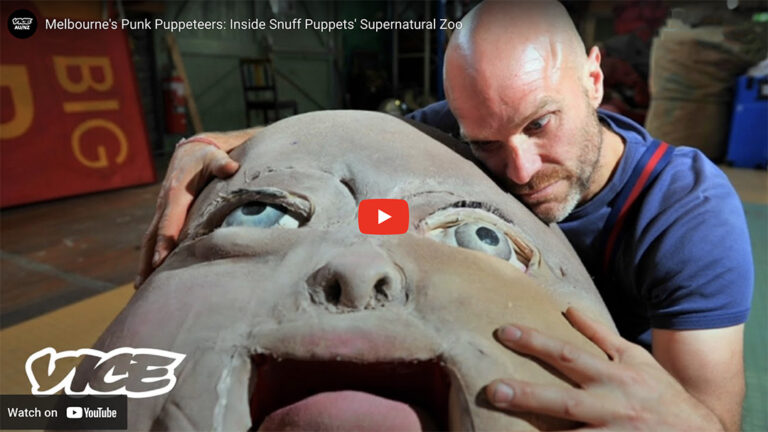 A big baby puppet head is hugged by Andy Freer