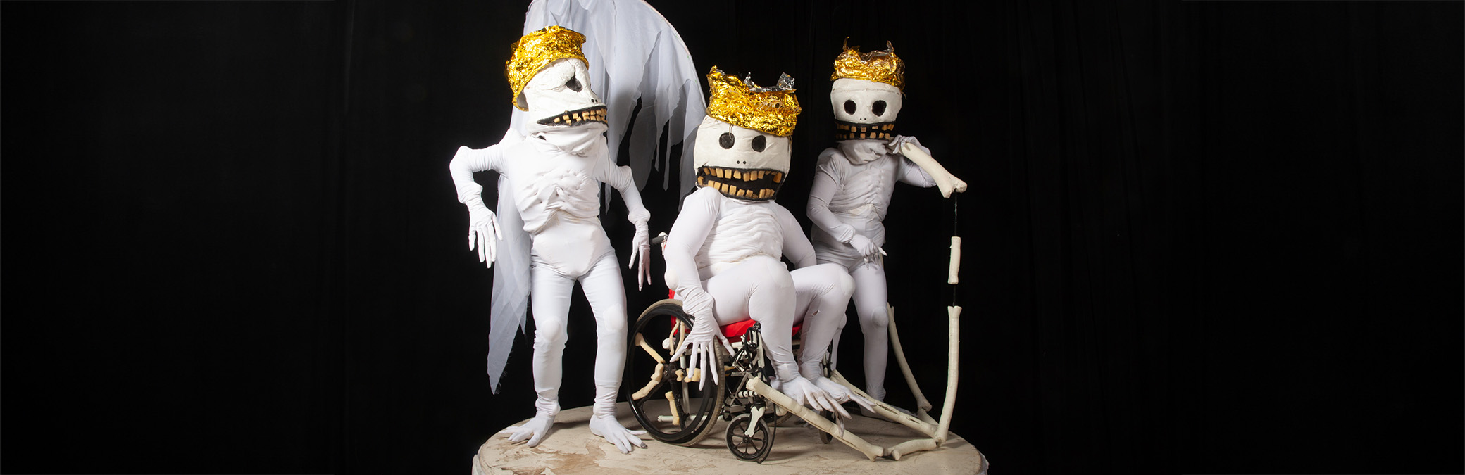 Photo of three Skullie puppets wearring gold crowns, one Skullie sits on a wheelchair.