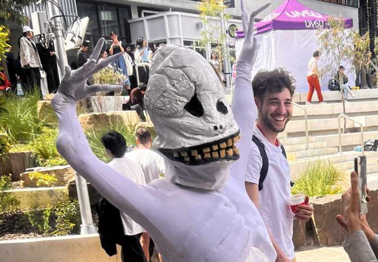 Skullie puppet with arms in the air while a person laughs